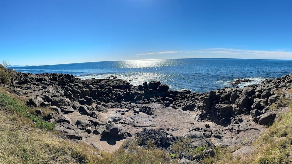 A coastal landscape with rocky terrain and a clear blue sky.