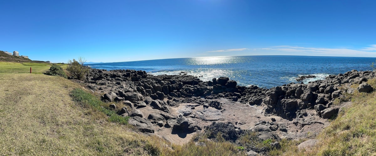 A coastal landscape with rocky terrain and a clear blue sky.