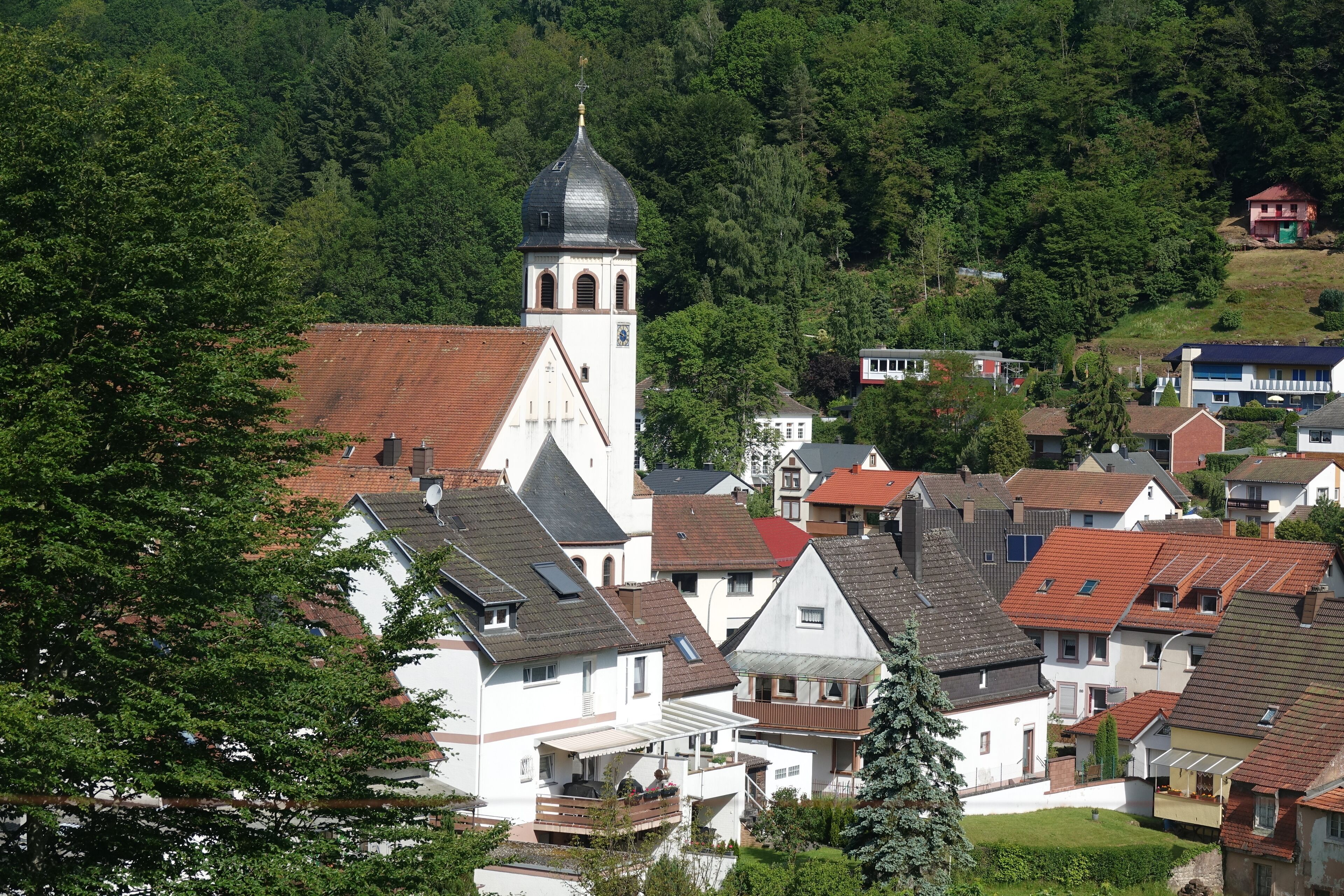 A village with a prominent church tower, surrounded by residential houses and lush greenery.