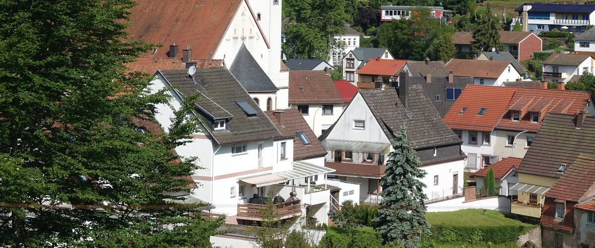 A village with a prominent church tower, surrounded by residential houses and lush greenery.
