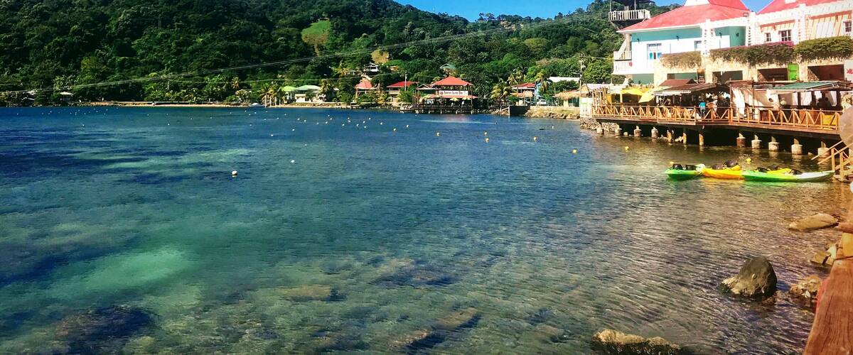 A coastal town with clear waters, a pier, and buildings with red roofs.