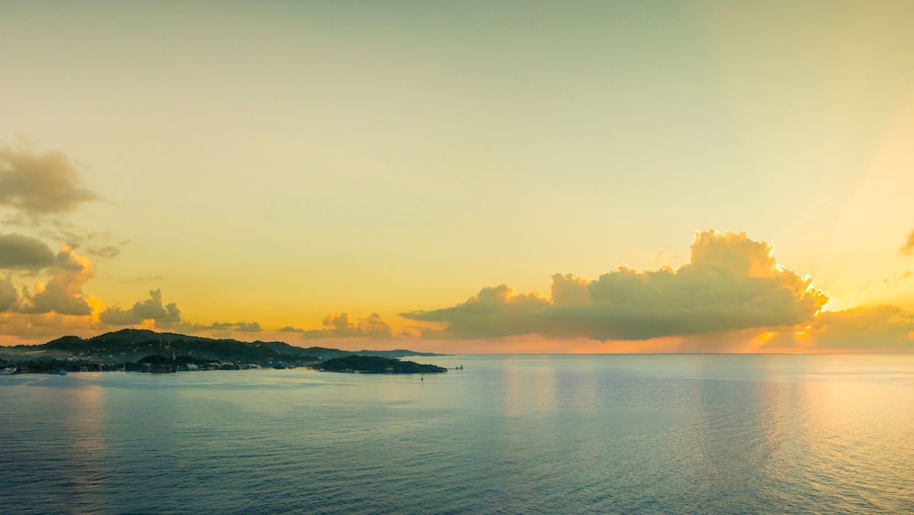 Ein ruhiges Meer bei Sonnenuntergang mit einer kleinen Insel und einem Schiff in der Ferne.