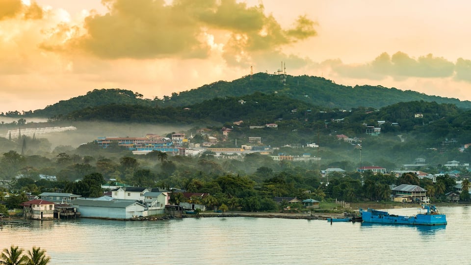 A coastal town with a blue boat on the water, surrounded by hills and houses.