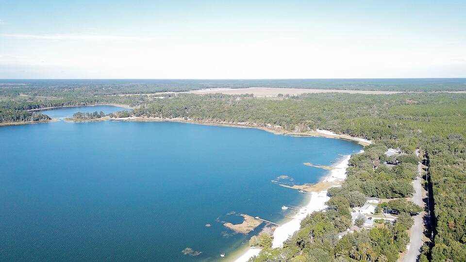 An aerial view of a large lake surrounded by dense forests and a few buildings along the shoreline.