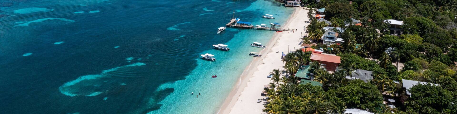 Aerial view of a coastal beach with crystal blue waters and white sand shoreline in Roatan Honduras