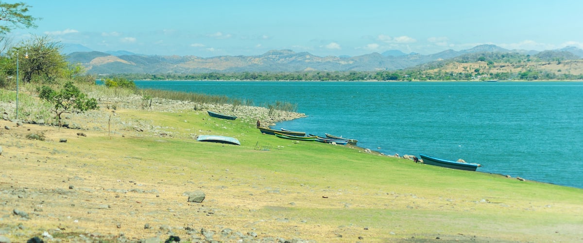 A lake with boats on the shore, surrounded by hills.
