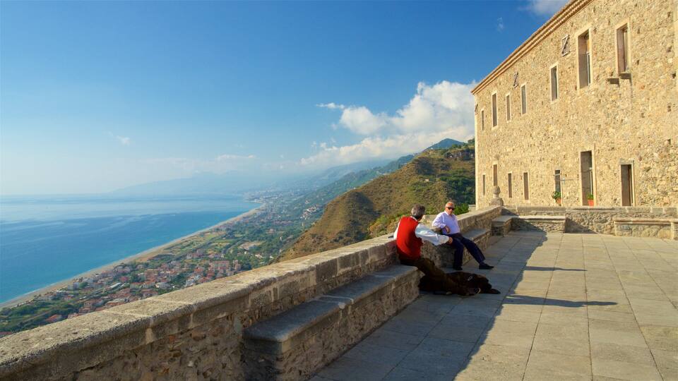 A stone building with a view of a coastal town and mountains in the background.