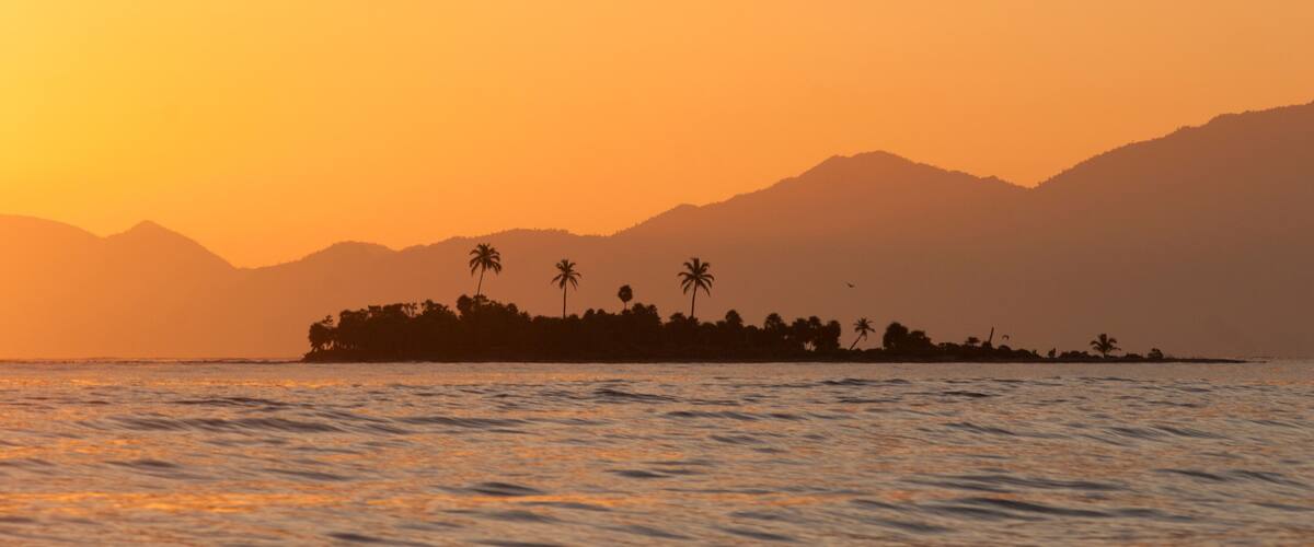 An island sits against the backdrop of Honduras' mountainous coast, Cayos Cochinos, Honduras.