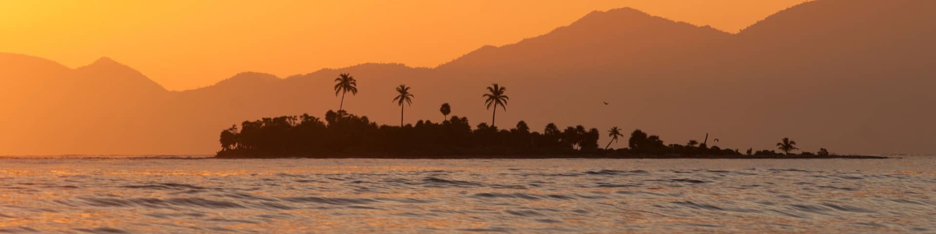 An island sits against the backdrop of Honduras' mountainous coast, Cayos Cochinos, Honduras.