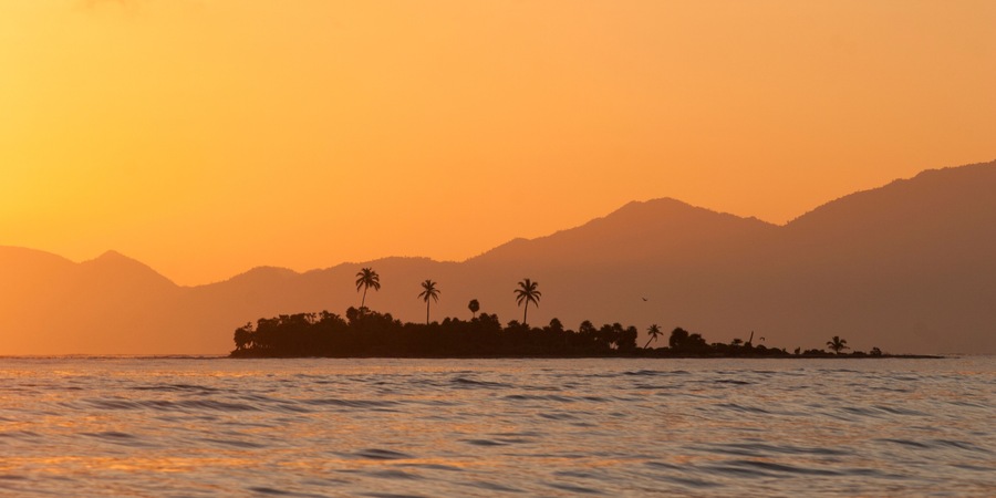 An island sits against the backdrop of Honduras' mountainous coast, Cayos Cochinos, Honduras.