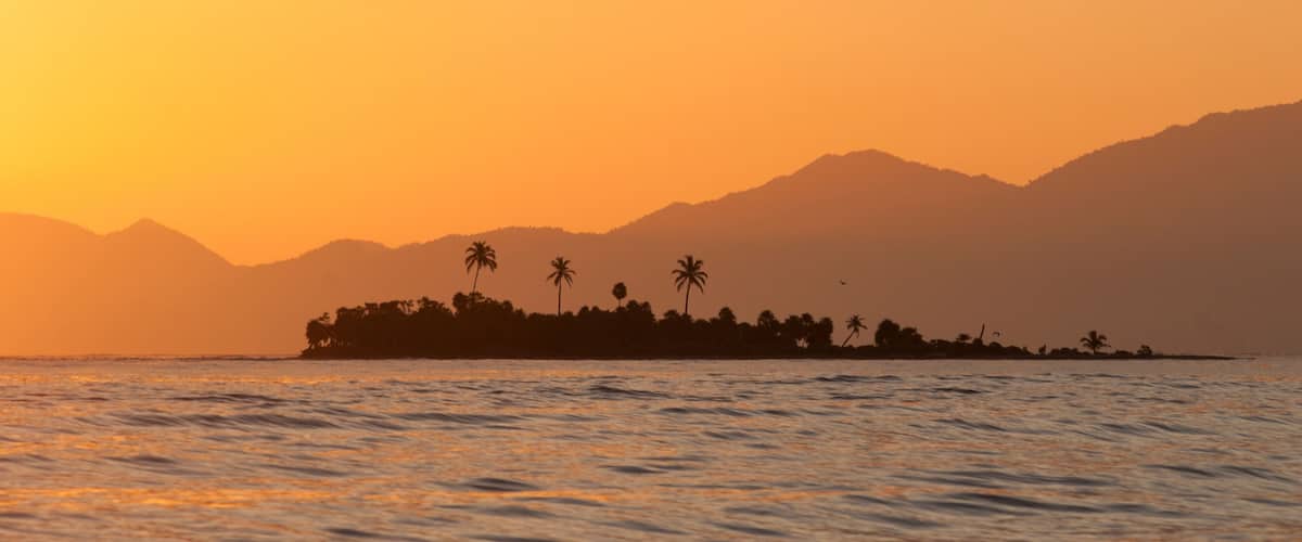 An island sits against the backdrop of Honduras' mountainous coast, Cayos Cochinos, Honduras.