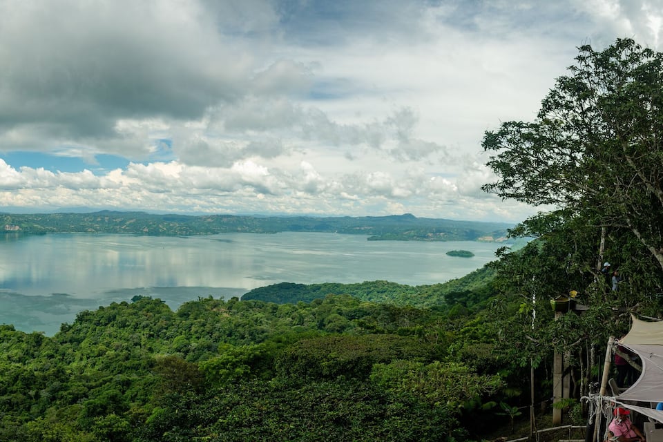 A lake surrounded by lush green hills and a cloudy sky.