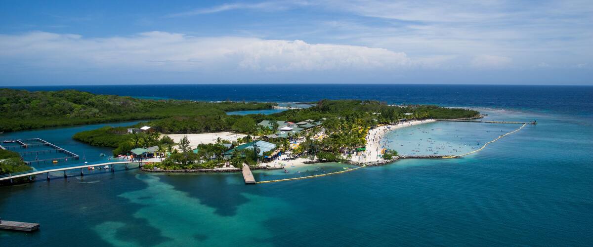 A tropical island with clear turquoise waters, a beach, and a bridge connecting to the mainland.