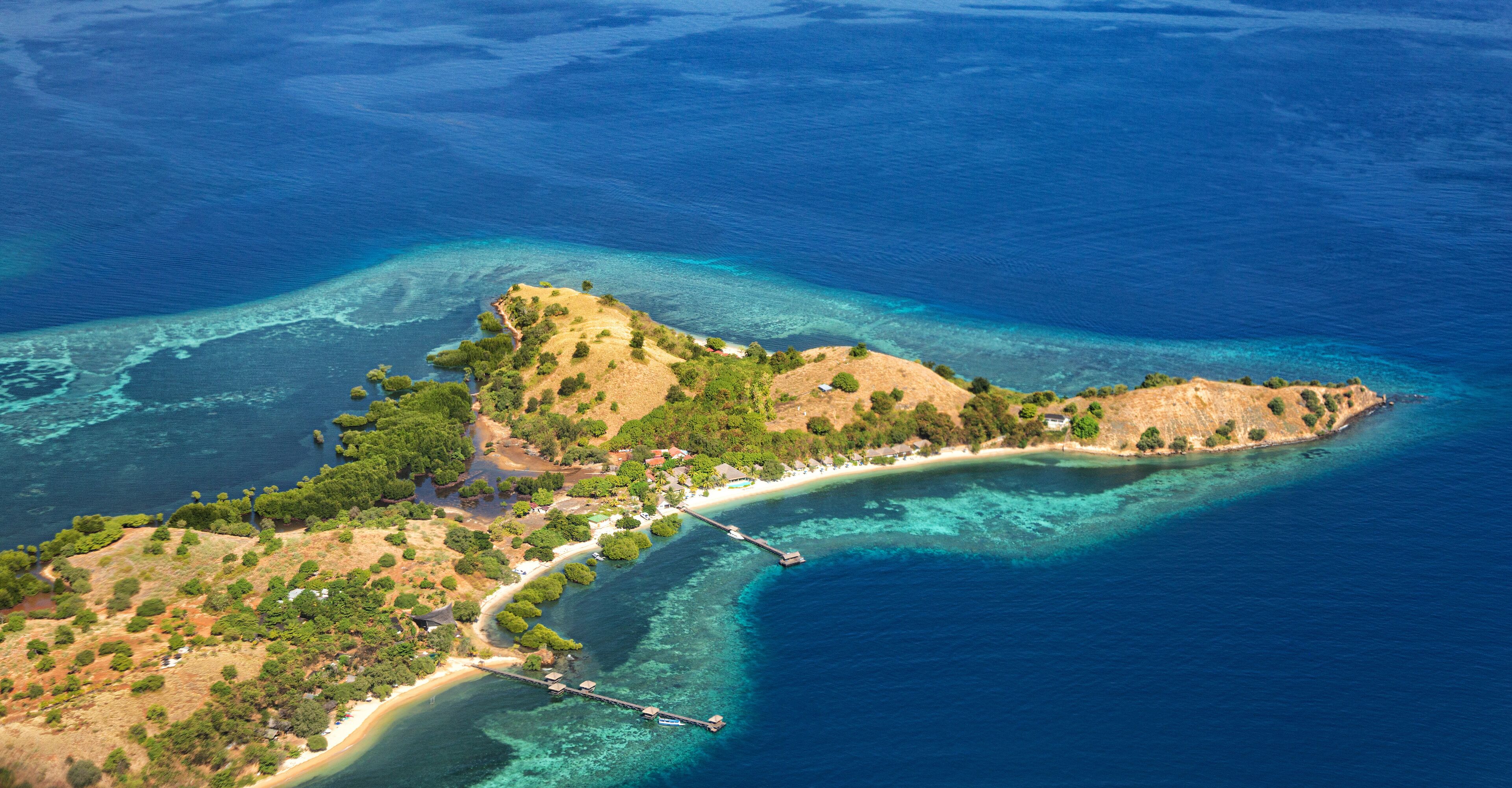 An aerial view of a coastal island with clear blue waters, a sandy beach, and a small pier.