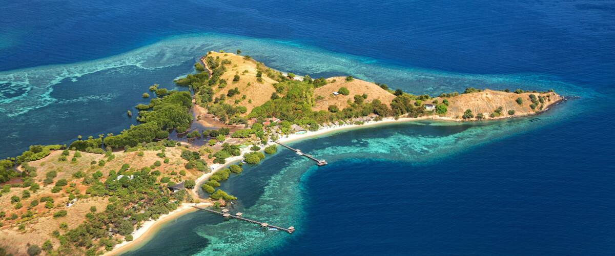 An aerial view of a coastal island with clear blue waters, a sandy beach, and a small pier.