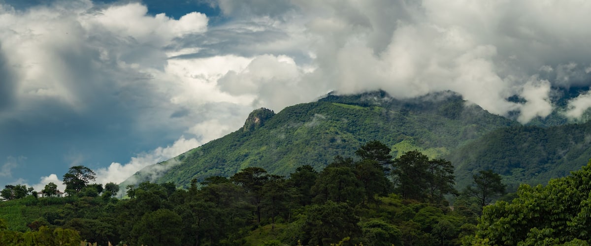 A mountain range with dense forest and clouds.
