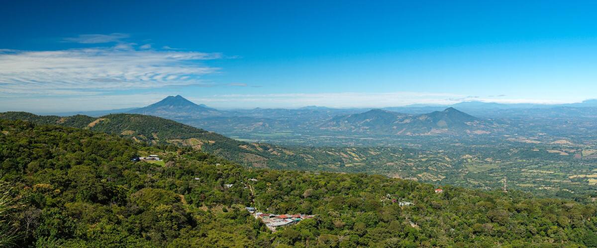 A mountainous landscape with dense forests, scattered houses, and a prominent mountain peak in the distance.