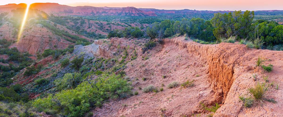 Un paisaje accidentado con un acantilado destacado y vegetación escasa.