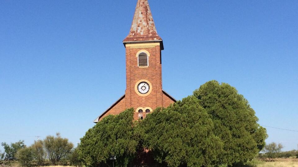 A church with a clock tower, surrounded by dry grass and trees.