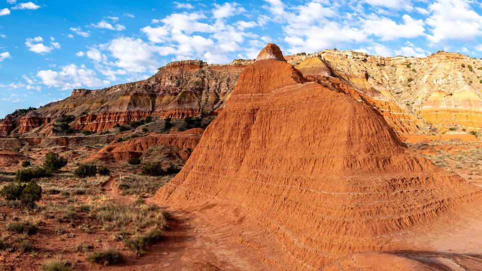 A large red rock formation with a clear sky and distant hills.