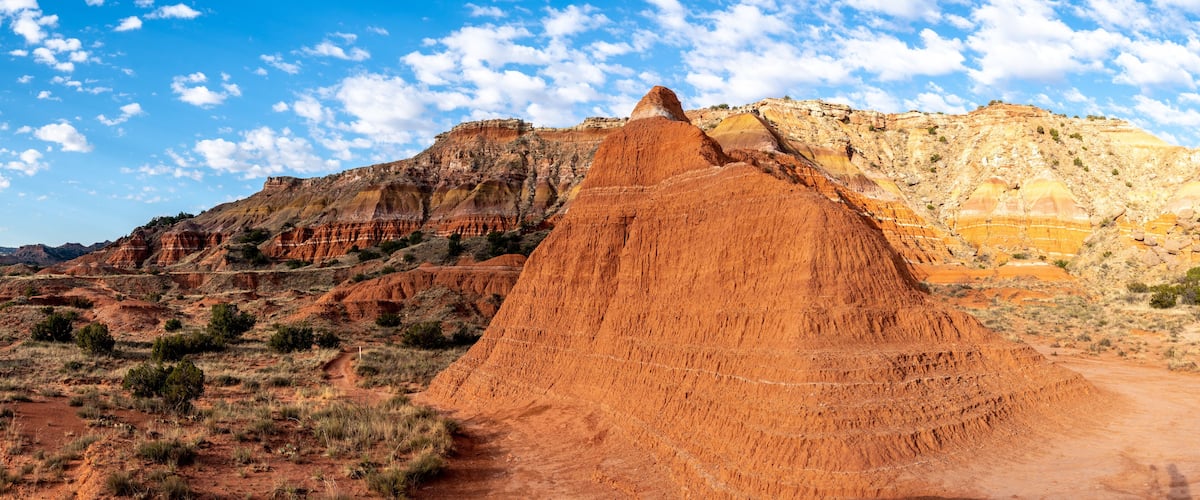A large red rock formation with a clear sky and distant hills.