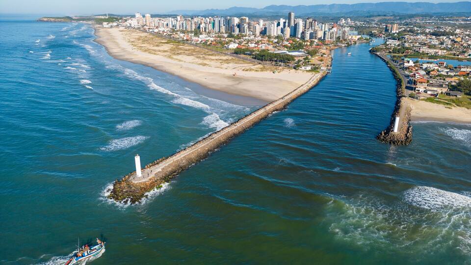 A coastal city with a long pier extending into the sea, a beach, and a densely built urban area in the background.