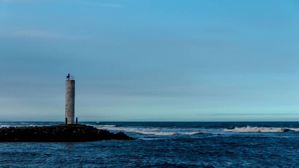 A lighthouse on a rocky outcrop with the ocean in the background.