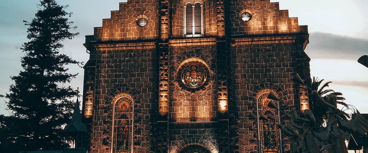 A church with a cross on top, a large circular window, and a statue of a tree.