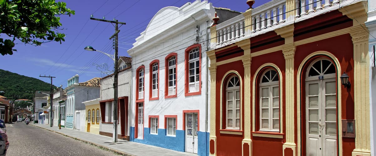A cobblestone street lined with colorful buildings, a clear blue sky, and a distant hill.