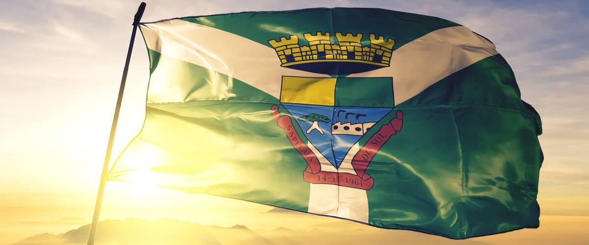 A flag with a crown, a shield, and the date "14-11-1961" against a sunrise sky.