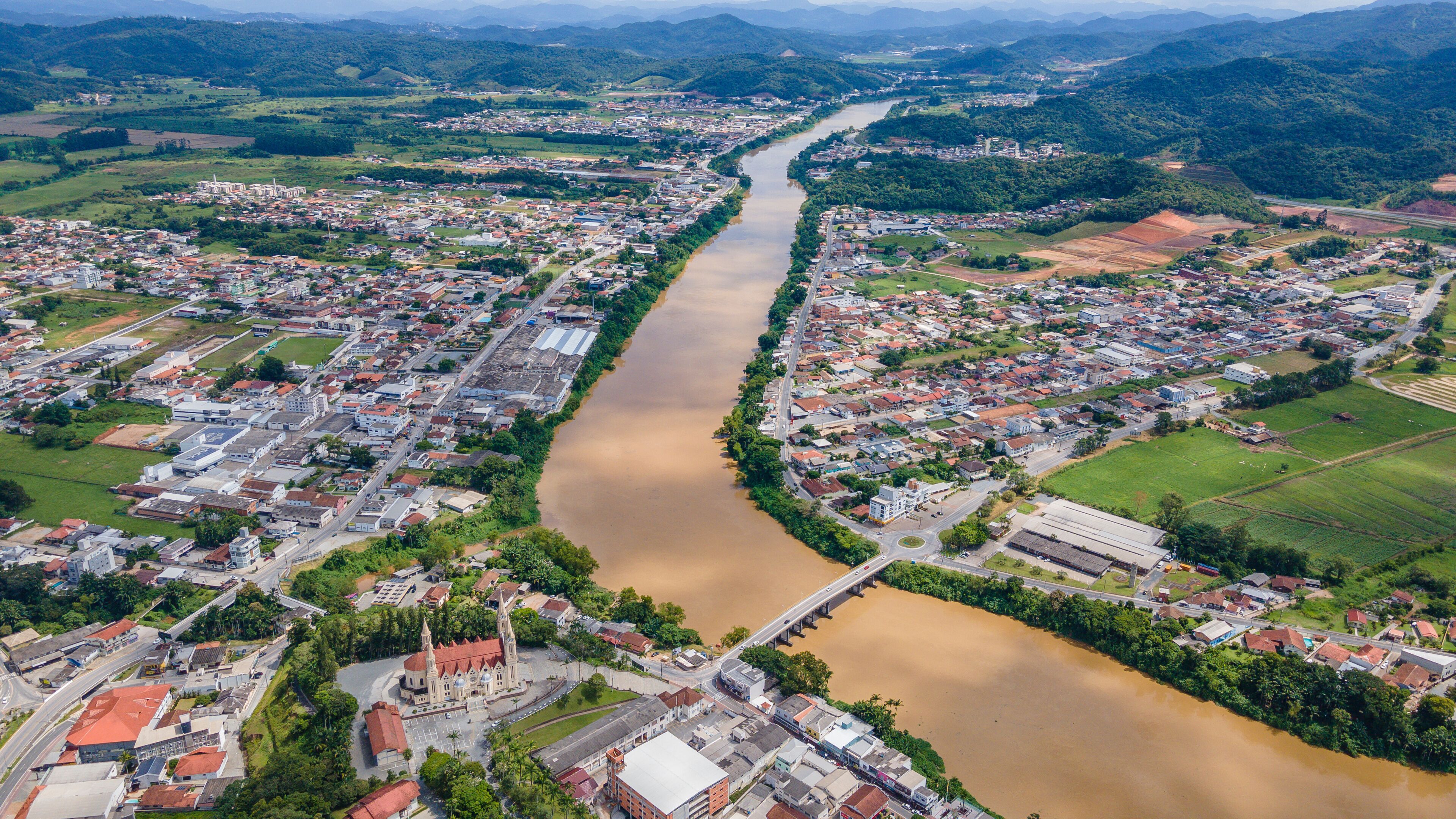 An aerial view of a river winding through a town with buildings and greenery.