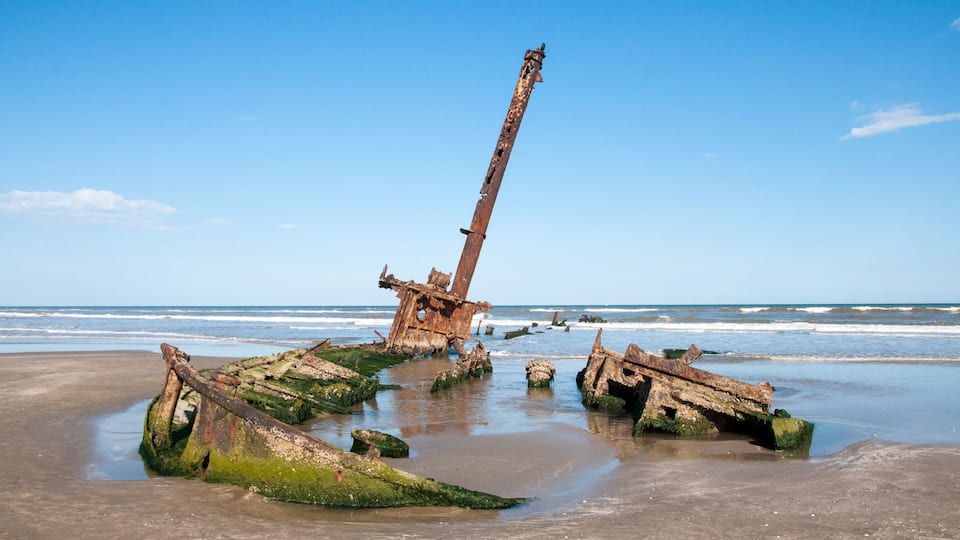 A beach with rusted shipwrecks and a clear blue sky.