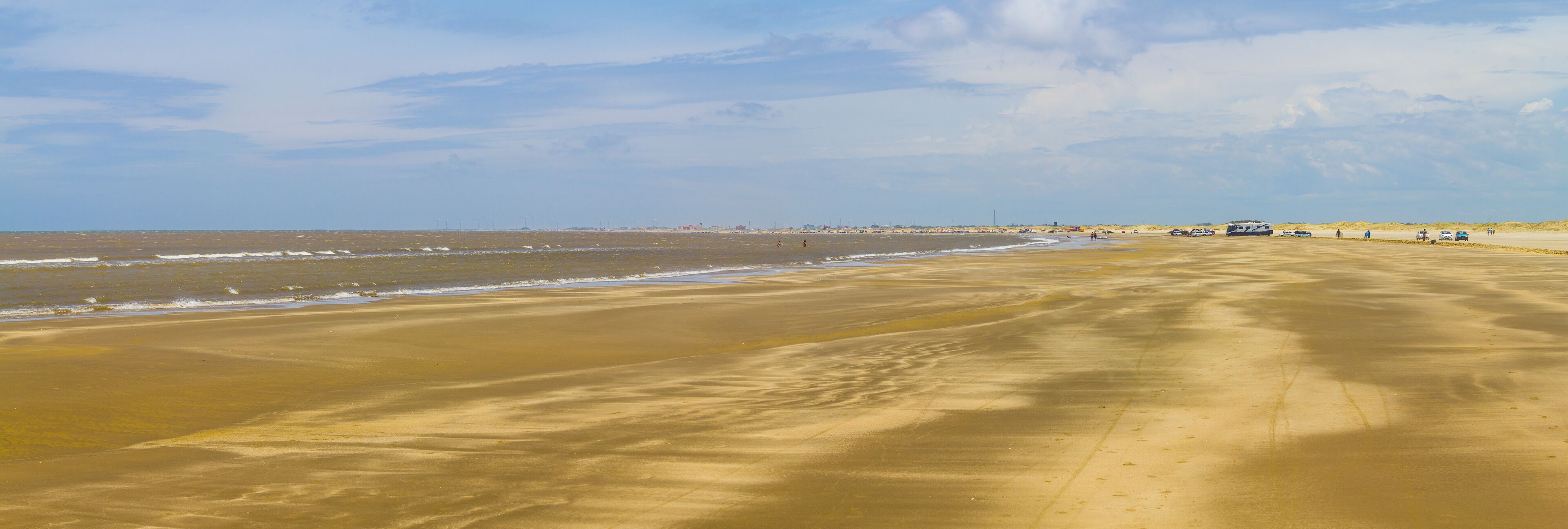 A wide sandy beach with gentle waves and a clear sky.