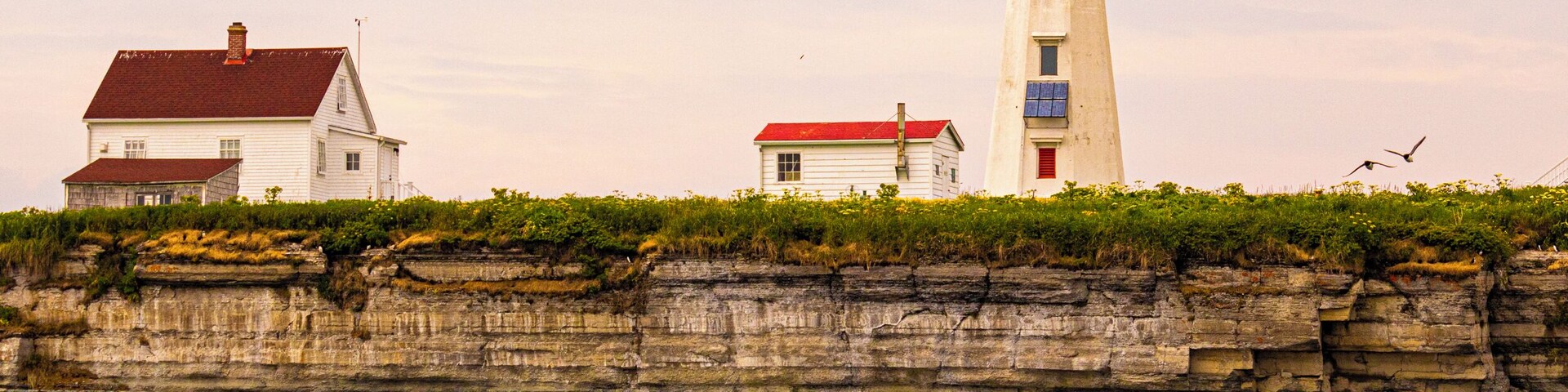 A coastal scene with a lighthouse, a white house with a red roof, and a rocky shoreline.