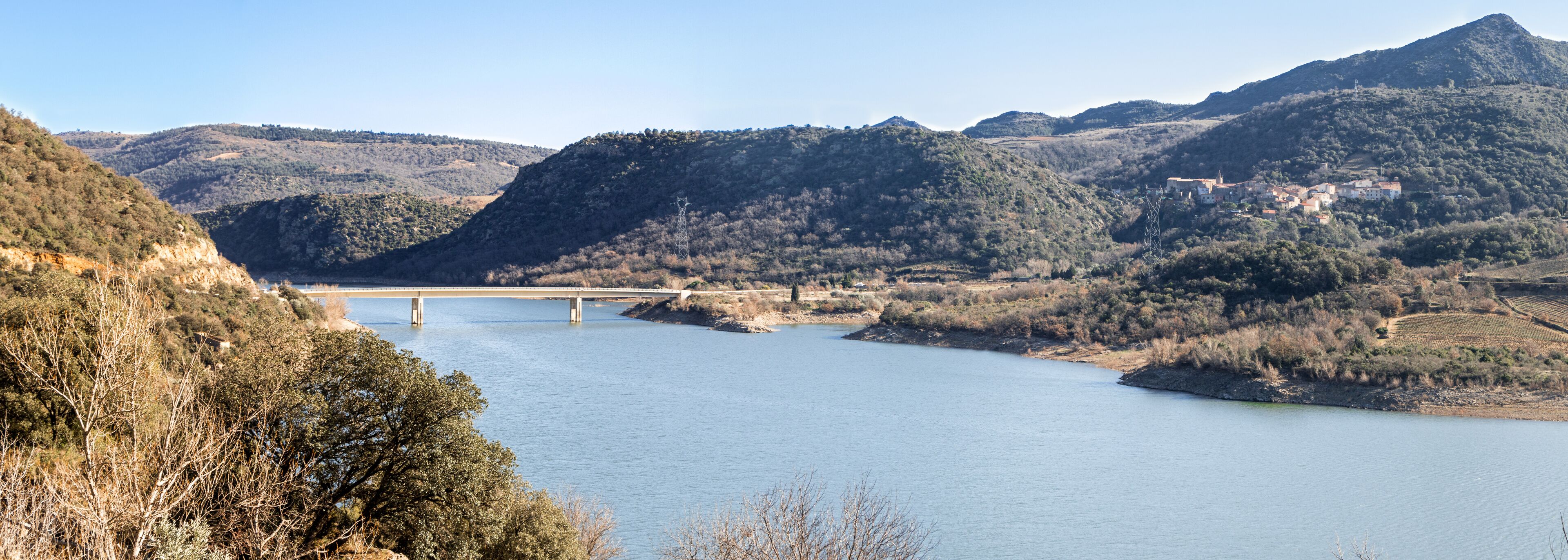 A river with a bridge, surrounded by hills and sparse vegetation.
