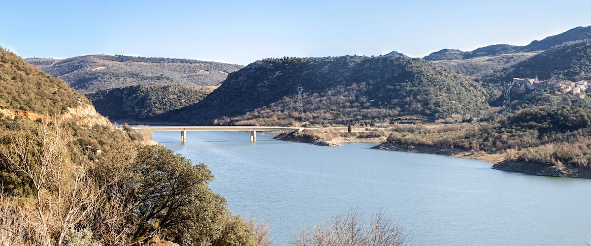A river with a bridge, surrounded by hills and sparse vegetation.