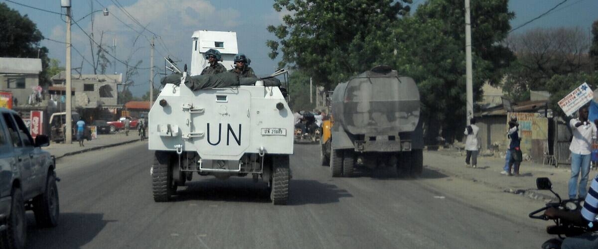 A UN armored vehicle on a street with buildings and trees.
