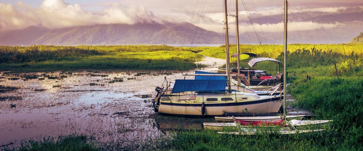 A sailboat docked in a marshy area with mountains in the background.