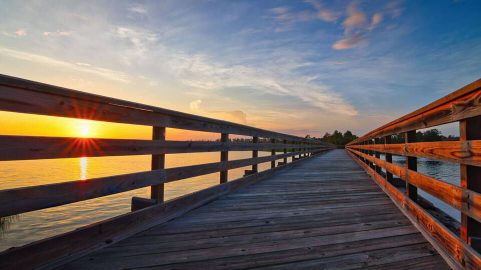 A wooden boardwalk leading to a sunset over water.