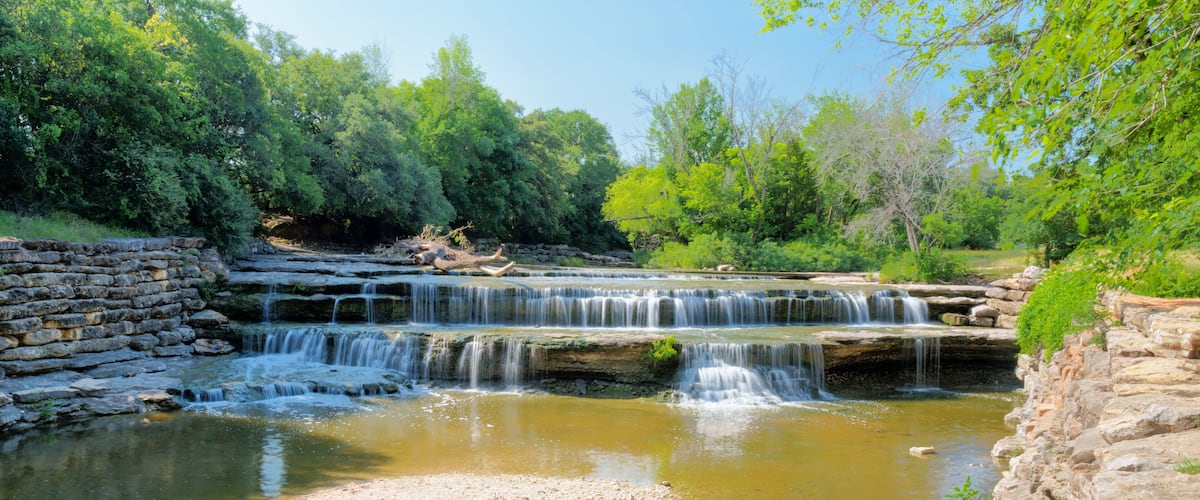 A multi-tiered waterfall surrounded by lush greenery and stone walls.