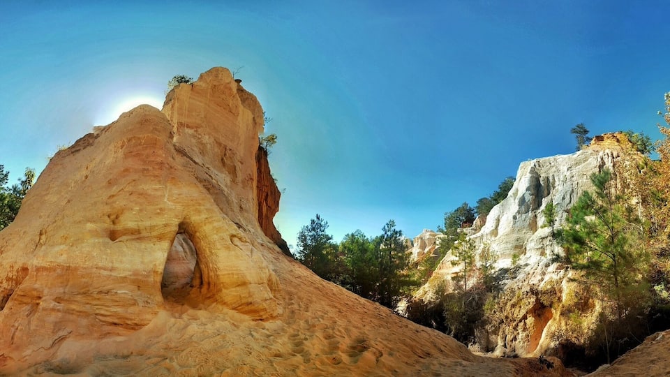 A large rock formation with a cave-like opening, surrounded by trees and other rock structures.