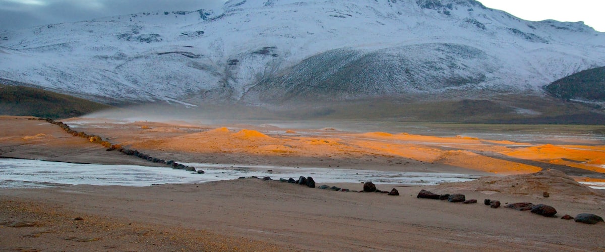 A snow-capped mountain, a river, and a rocky shoreline.