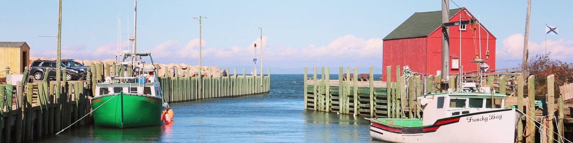 A coastal harbor with wooden piers, a red building, and two boats named 'Frenchy Bay'.
