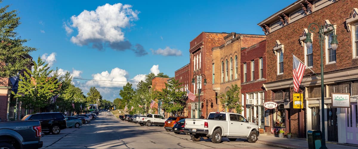 A street lined with brick buildings, parked cars, and American flags.