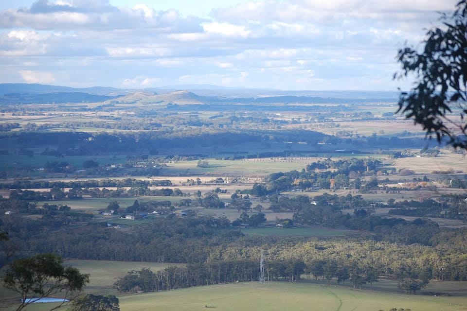 A rural landscape with rolling hills, scattered trees, and a few buildings.