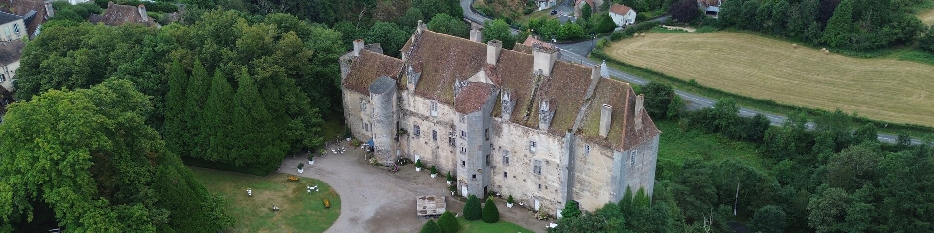 Vista aérea de un castillo histórico rodeado de abundante vegetación y un pequeño pueblo.