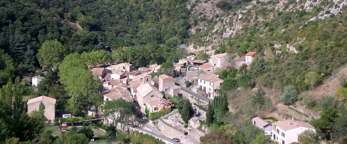 A village nestled in a valley surrounded by forested hills, with a historic castle on a hilltop.