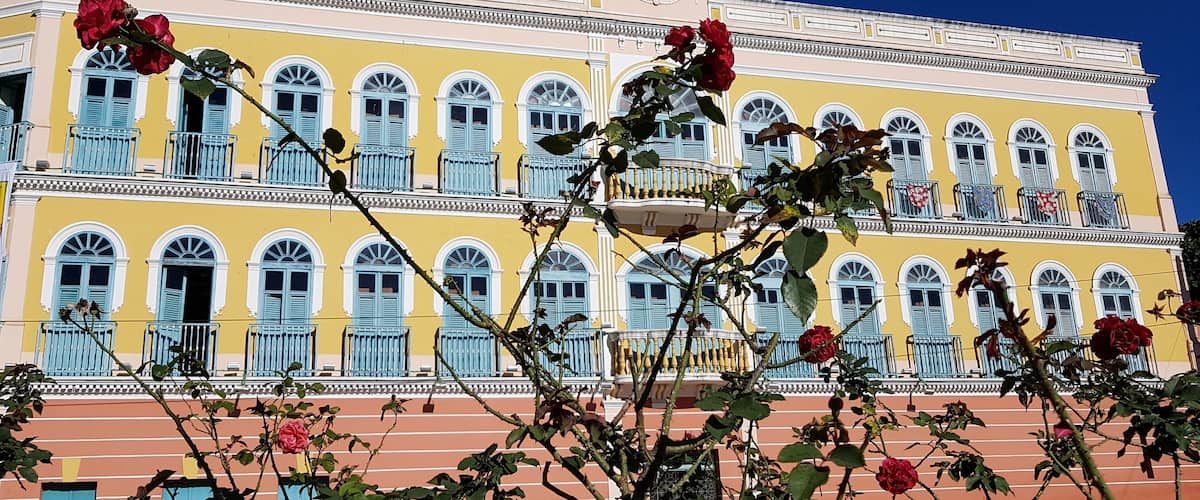 A yellow building with blue shutters and a balcony, surrounded by roses.