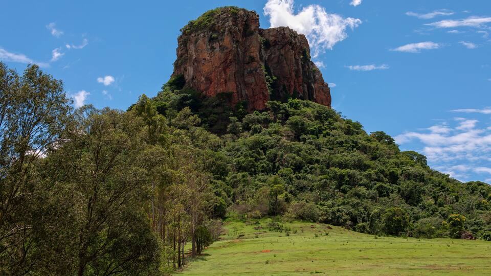 A prominent rocky mountain peak surrounded by lush green forest and a clear blue sky.