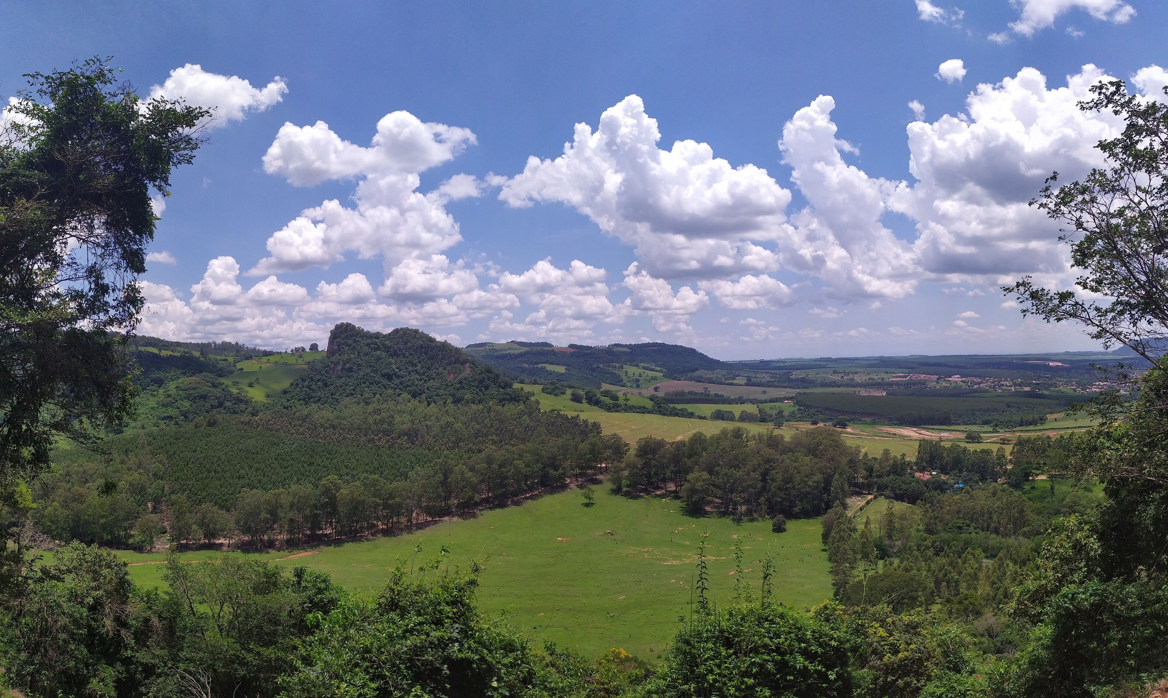 A lush green valley with rolling hills, a clear blue sky, and scattered clouds.